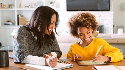 Grandmother And Granddaughter Sitting At Table At Home Drawing Picture On Digital Tablet With Stylus