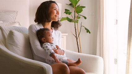 Mother Sitting On Chair In Bedroom Holding Smiling Baby Son