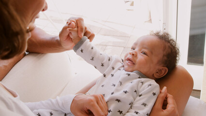 Mother Sitting On Chair In Bedroom Holding Smiling Baby Son
