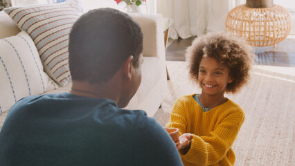 Daughter Giving Father Clay Pot That She Has Made Herself Sitting On Sofa At Home