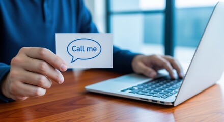 Man working on laptop holding call me card indicating connection and communication