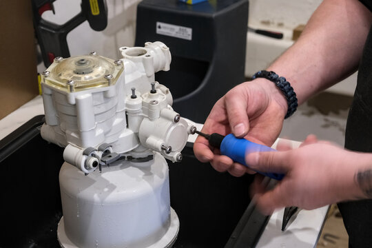 Hand tightens screw on water softener body, showing active maintenance with motion blur in workshop.