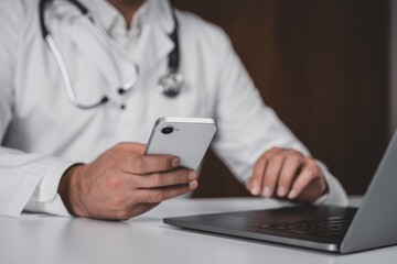 Doctor using smartphone and laptop for online teleconsultation on healthcare technology background in modern medical office workspace concept.