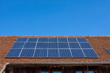 Fototapeta premium Solar Panels on Roof Against Clear Blue Sky for Renewable Energy