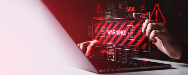 Cybersecurity warning alert on digital screen with hands typing on laptop, concept of data breach and malware attack on dark red background.