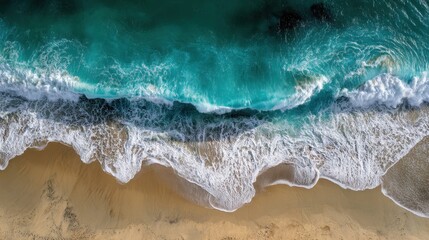 Aerial view of turquoise ocean waves crashing on the sandy shore.