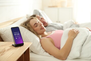 Lovely couple lying in bed at home, focus on smartphone with alarm clock app