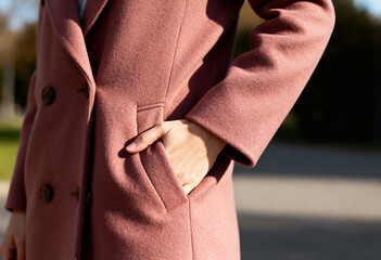 Woman's hand in pocket of dusty pink wool coat outdoors. Close-up of double-breasted winter jacket texture. Autumn fashion detail