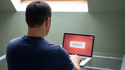 Man using laptop with large donate button on screen while sitting at glass desk in bright modern home office interior