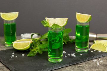 Sweet refreshing mint liqueur, with ice and mint leaves on table background, Shots with lime slice and mint flat lay