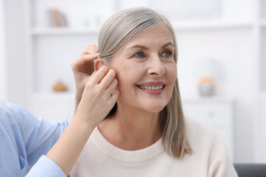 Woman putting hearing aid into her mother's ear at home, closeup