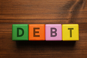 Debt word made of cubes with letters on wooden table, top view