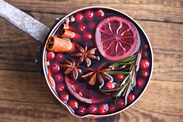 Copper pot with red mulled wine with slices of orange, cinnamon, star anise, rosemary and cranberries on wooden table. Food photography