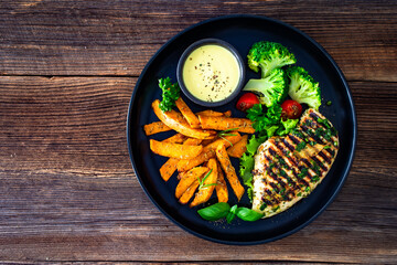 Grilled chicken breast, sweet potato fries with barbecue sauce and boiled broccoli on wooden table
