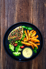 Grilled chicken breast, sweet potato fries with barbecue sauce and boiled broccoli on wooden table
