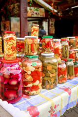 Colorful Pickled vegetables stacked in glass jars on table for sale