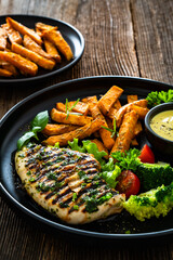 Grilled chicken breast, sweet potato fries with barbecue sauce and boiled broccoli on wooden table
