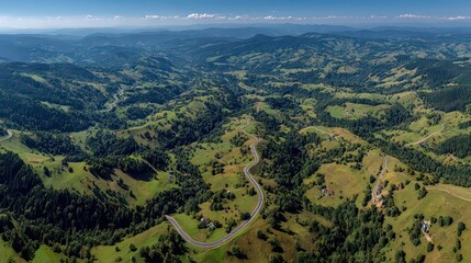Fototapeta premium Expansive Green Mountain Landscape With Winding Road And Distant Hills Under Blue Sky