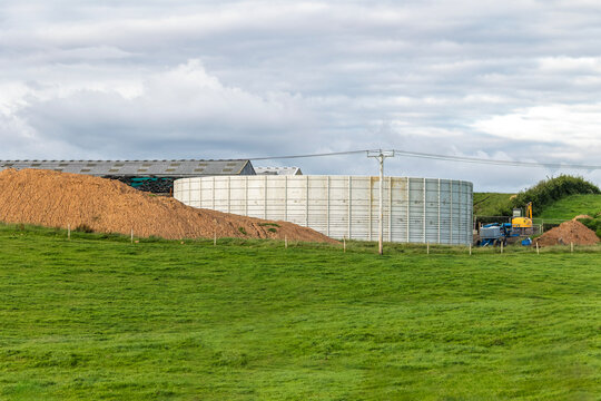 Large slurry storage tank on cattle farm in rural landscape in front of buildings and beside excavated dirt