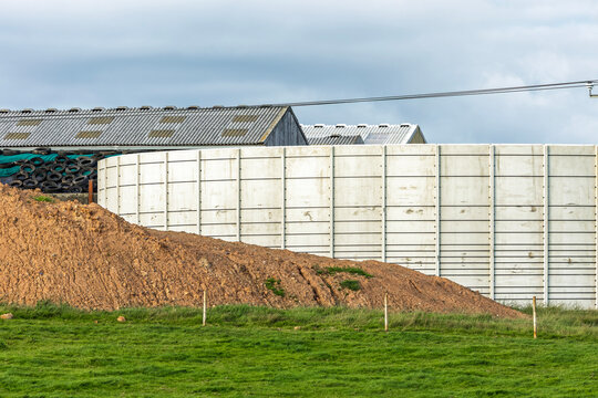 Large slurry storage tank on cattle farm in rural landscape in front of buildings and beside excavated dirt