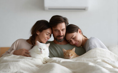 Affectionate trio including man woman and friend cuddling in bed with two cats while feeling cozy peaceful and happy relaxing under blanket enjoying warm comfortable morning together in bedroom