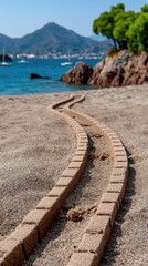 Obraz premium Sand pathway leads to calm blue water and rocky shore under a clear sky, inviting exploration and relaxation at the beach during warm daylight