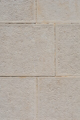 A vertical close-up of an exterior wall featuring light gray, rectangular, textured stone blocks stacked in a neat masonry pattern