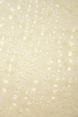 A high-angle, vertical full-frame background of white liquid milk covered in a dense layer of small, frothy, reflective air bubbles