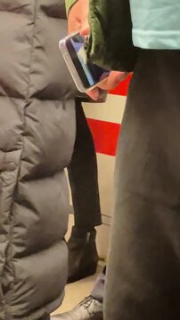 Passenger Checking Phone And Holding Handbag, Red Platform Stripes In Background, Scene Of Routine Urban Commute Vertical shot taken on mobile device