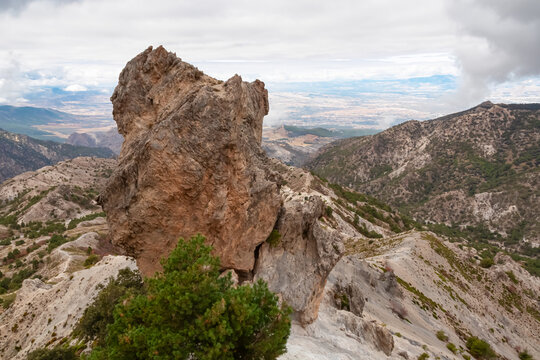 A massive limestone rock formation dominates the foreground against a backdrop of arid valleys and distant horizons, showcasing the rugged terrain of Sierra Nevada near Cerro del Trevenque in Granada.