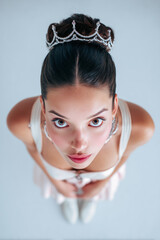 Young girl in a white dress with a tiara gazes upward in a studio setting against a plain background during a photoshoot