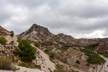 Scattered green pines dot the eroded limestone slopes of Cerro del Trevenque, creating a textural contrast in the wild landscape of Sierra Nevada, Spain, under a heavy and overcast autumn sky.