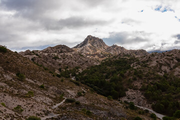A winding hiking trail cuts through the eroded valleys beneath Cerro del Trevenque, guiding trekkers through the wild landscape of Sierra Nevada, Spain, under a dramatic and cloudy atmosphere.