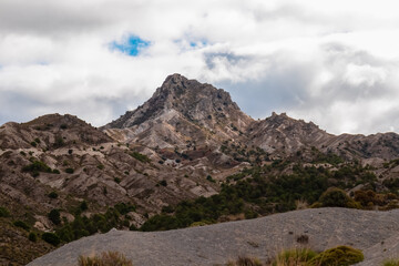 The rugged limestone peak of Cerro del Trevenque rises above arid slopes, dominating the cloudy skyline of Sierra Nevada near Granada, Spain, and highlighting the dramatic geological nature.