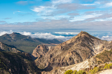 The rugged peak of Cerro del Trevenque dominates the deep valleys, rising above rolling clouds in Sierra Nevada, Granada, highlighting the arid beauty of the dramatic Spanish mountain landscape.
