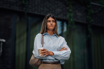 Businesswoman holding coffee cup and crossing arms in front of office building