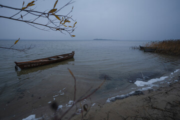 Old rural wooden, fishing boat is moored on the shore of a lake. A gloomy windy day