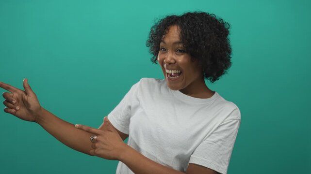Woman smiling and pointing finger to the right wearing a white t shirt in a green studio; joy and enthusiasm.