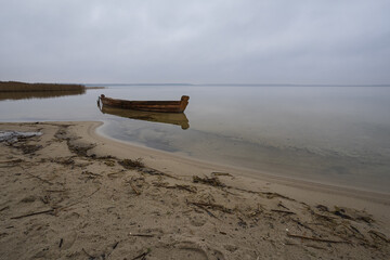 Old rural wooden, fishing boat is moored on the shore of a lake. A gloomy windy day