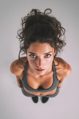 Woman with curly hair in fitness attire stands straight looking up, showcasing determination and strength during a workout session indoors