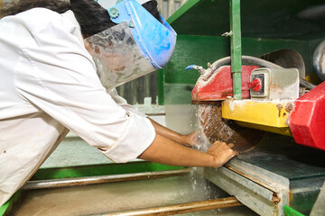 Worker cutting stone with circular saw in workshop