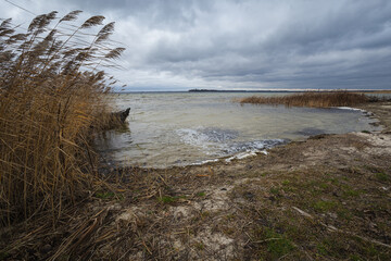 Old rural wooden, fishing boat is moored on the shore of a lake. A gloomy windy day