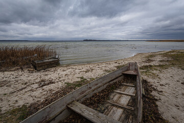 Old rural wooden, fishing boat is moored on the shore of a lake. A gloomy windy day
