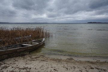 Old rural wooden, fishing boat is moored on the shore of a lake. A gloomy windy day