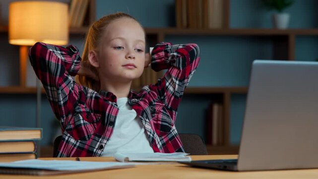 Caucasian little child girl kid looking in laptop e-learning at home studying distant holding hands behind head relaxing daughter relaxed leaning chair watch study learn lesson in computer at evening