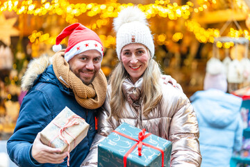 Couple enjoying Bavarian Christmas market vibes holding gifts and smiling beneath shining holiday lights
