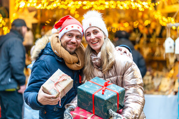 Couple enjoying holiday spirit at a Bavarian Christmas market holding colorful gifts and sharing warm smiles