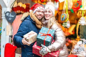 Joyful couple walking through a Bavarian Christmas market holding wrapped presents under warm glowing lights