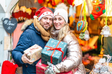 Happy couple enjoying festive lights at a Bavarian Christmas market holding colorful holiday gifts