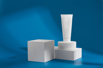 White tube of cosmetic product sits on geometric shapes against blue backdrop